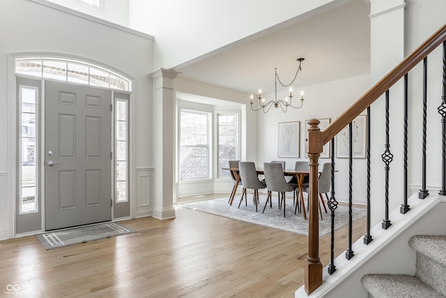 entrance foyer featuring light wood finished floors, stairs, an inviting chandelier, and decorative columns