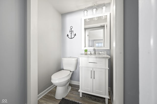 half bath with vanity, toilet, wood finished floors, and baseboards