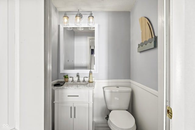 half bath with a textured ceiling, toilet, and vanity