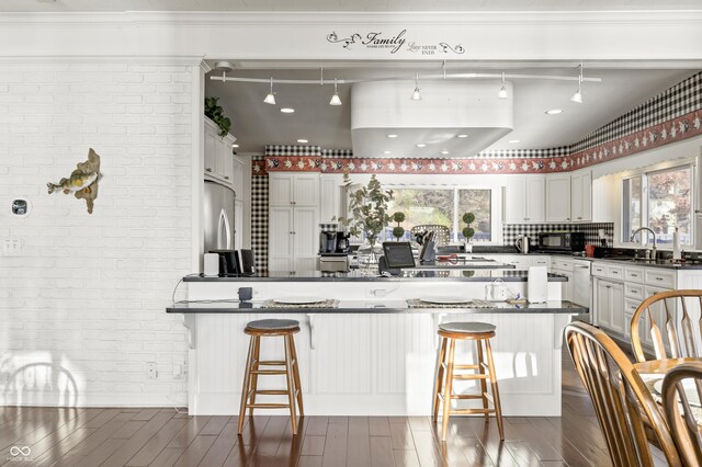 kitchen with brick wall, a kitchen bar, and dark wood-style flooring