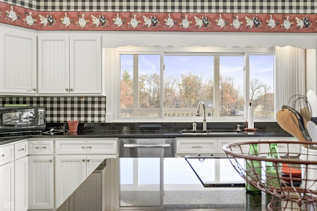 kitchen featuring dark countertops, dishwasher, plenty of natural light, white cabinetry, and a sink