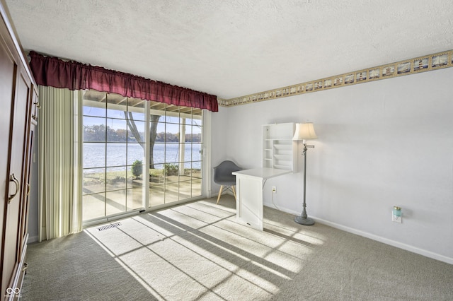 unfurnished office featuring visible vents, a water view, carpet, and a textured ceiling