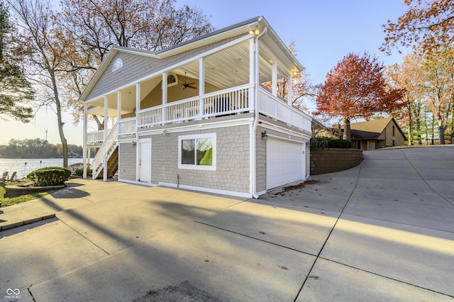 view of property exterior featuring stairway, a ceiling fan, driveway, an attached garage, and a water view