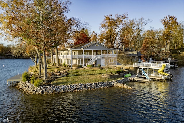 back of property with stairway, a water view, and a lawn