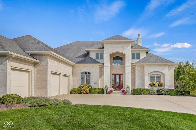 french country style house with a front lawn, roof with shingles, concrete driveway, an attached garage, and brick siding