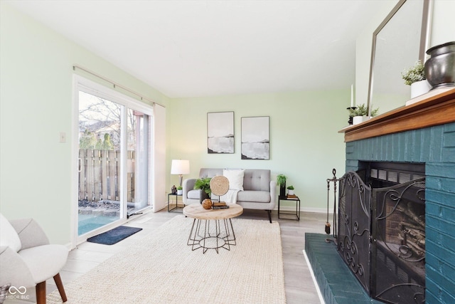 living room featuring a brick fireplace, wood finished floors, and baseboards