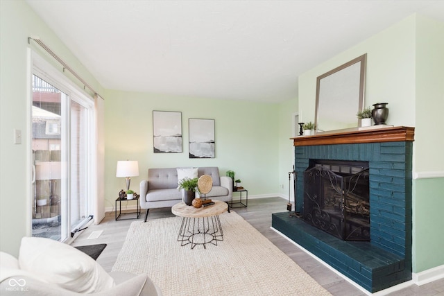 living room with a brick fireplace, baseboards, and wood finished floors