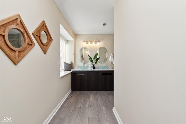 hallway featuring visible vents, baseboards, and light wood finished floors