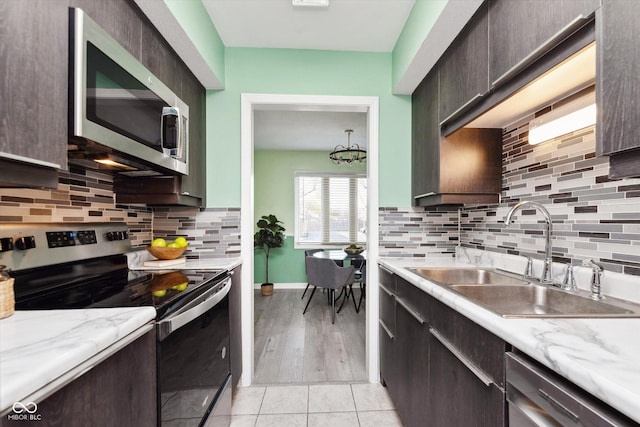 kitchen featuring a sink, dark brown cabinetry, appliances with stainless steel finishes, light tile patterned floors, and decorative backsplash