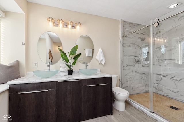 bathroom with a marble finish shower, toilet, and a sink