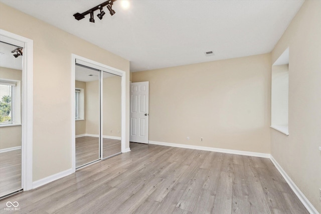 unfurnished bedroom featuring visible vents, wood finished floors, a closet, rail lighting, and baseboards