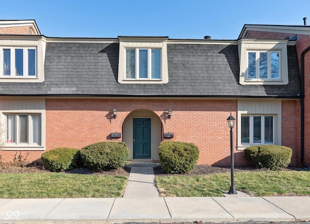 view of front facade featuring mansard roof, brick siding, and a shingled roof