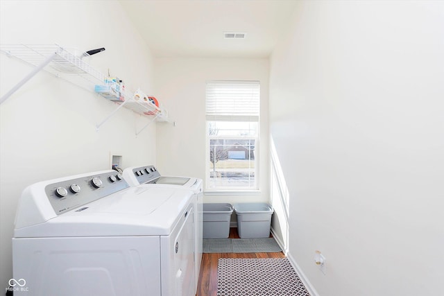 clothes washing area featuring visible vents, wood finished floors, baseboards, laundry area, and washing machine and clothes dryer