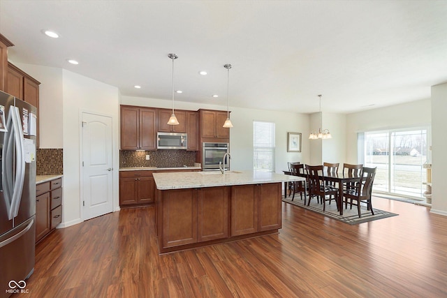 kitchen with pendant lighting, decorative backsplash, dark wood-style flooring, stainless steel appliances, and a kitchen island with sink