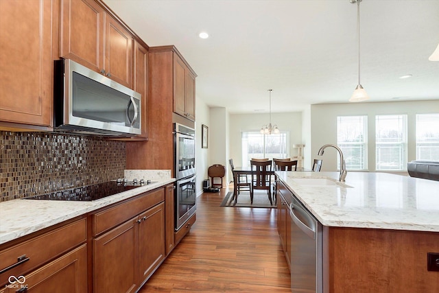 kitchen featuring brown cabinets, a sink, backsplash, dark wood-style floors, and appliances with stainless steel finishes