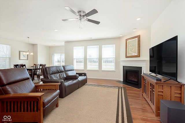 living area with a fireplace with flush hearth, recessed lighting, light wood finished floors, baseboards, and ceiling fan