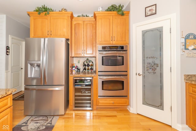 kitchen with wine cooler, appliances with stainless steel finishes, light wood-style flooring, and light stone countertops