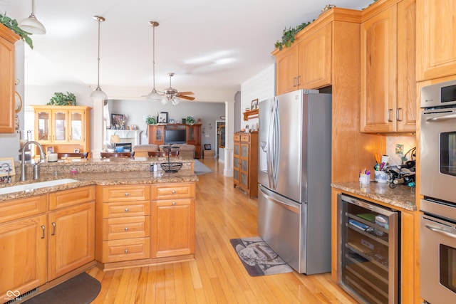 kitchen featuring wine cooler, a fireplace, light wood-style floors, stainless steel appliances, and a sink