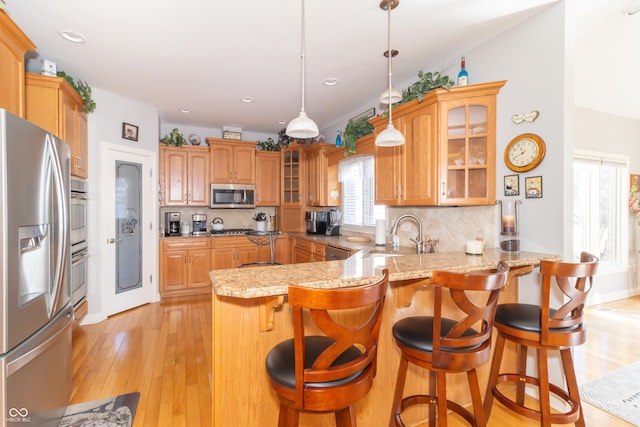 kitchen featuring backsplash, glass insert cabinets, light wood-type flooring, appliances with stainless steel finishes, and a peninsula