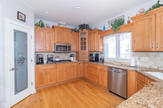 kitchen with light stone countertops, tasteful backsplash, appliances with stainless steel finishes, and light wood finished floors