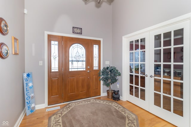 foyer featuring visible vents, baseboards, french doors, a high ceiling, and wood finished floors