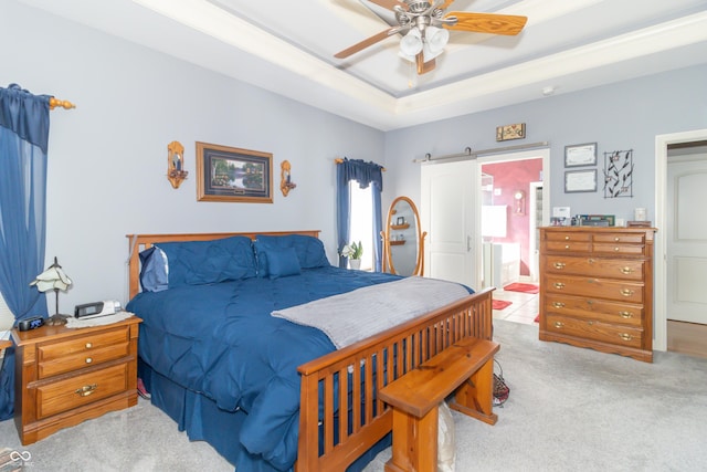 bedroom featuring connected bathroom, a barn door, carpet flooring, a raised ceiling, and a ceiling fan