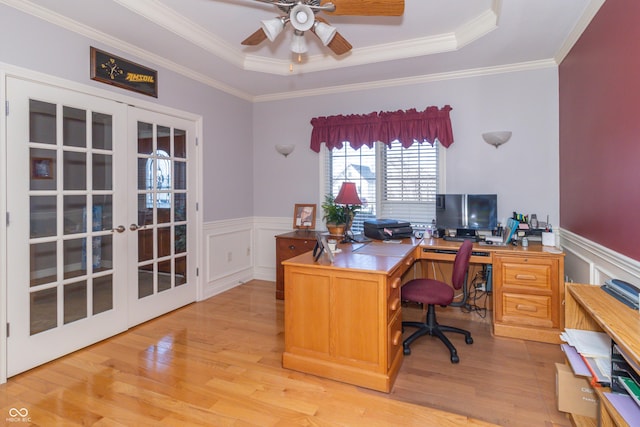 home office featuring a tray ceiling, light wood-style flooring, french doors, and a wainscoted wall