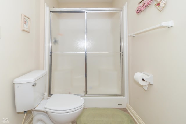 bathroom with a shower with door, baseboards, and toilet