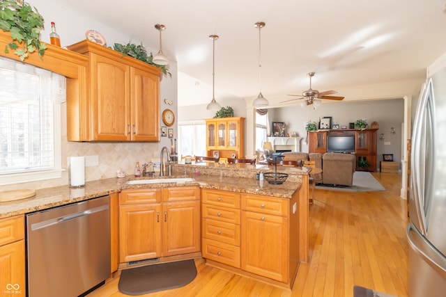 kitchen with a peninsula, a sink, appliances with stainless steel finishes, light wood-type flooring, and backsplash