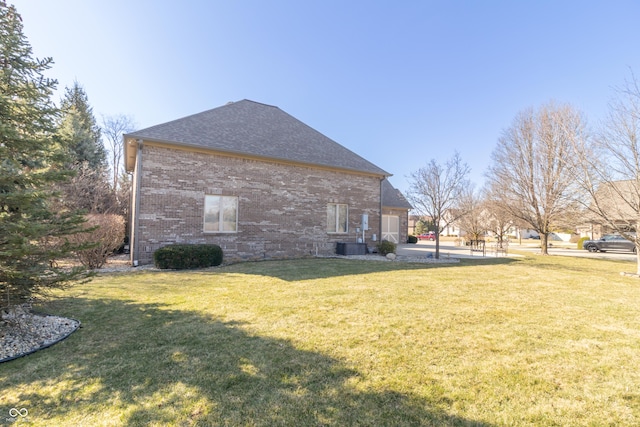 view of side of property featuring brick siding, roof with shingles, and a lawn