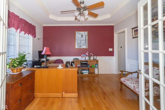 home office with ornamental molding, wainscoting, light wood-style flooring, a raised ceiling, and a ceiling fan