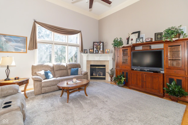 living area with a tile fireplace, crown molding, and ceiling fan