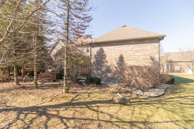 view of side of property featuring a lawn, brick siding, and roof with shingles