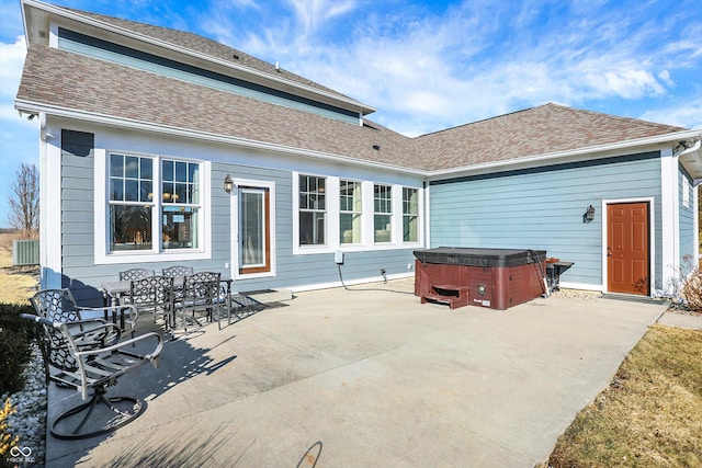 back of property with a patio, roof with shingles, and a hot tub