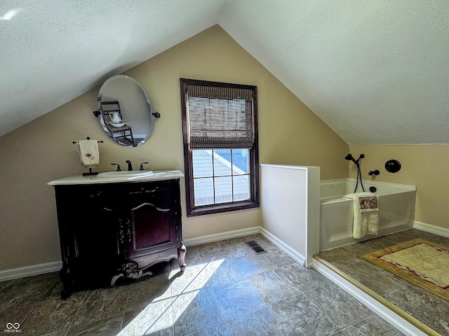 bathroom with visible vents, a textured ceiling, baseboards, a bath, and vanity