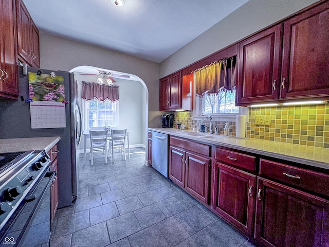 kitchen featuring gas stove, arched walkways, stainless steel dishwasher, tasteful backsplash, and reddish brown cabinets