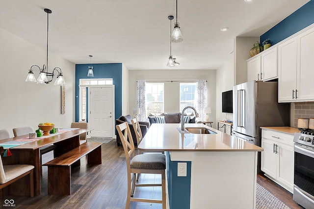 kitchen with a kitchen island with sink, a sink, tasteful backsplash, dark wood finished floors, and appliances with stainless steel finishes