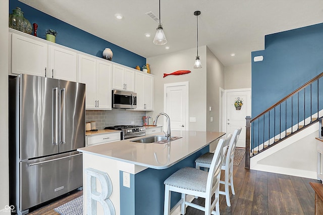 kitchen featuring a center island with sink, dark wood finished floors, a sink, white cabinets, and appliances with stainless steel finishes