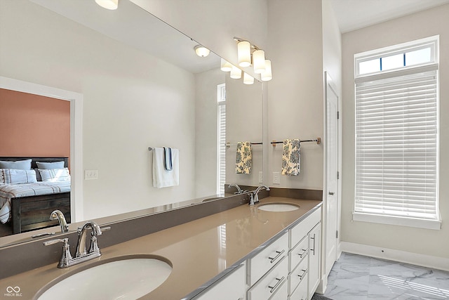 ensuite bathroom featuring a sink, baseboards, marble finish floor, and double vanity