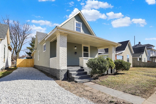 view of front of home with brick siding, a porch, driveway, and fence