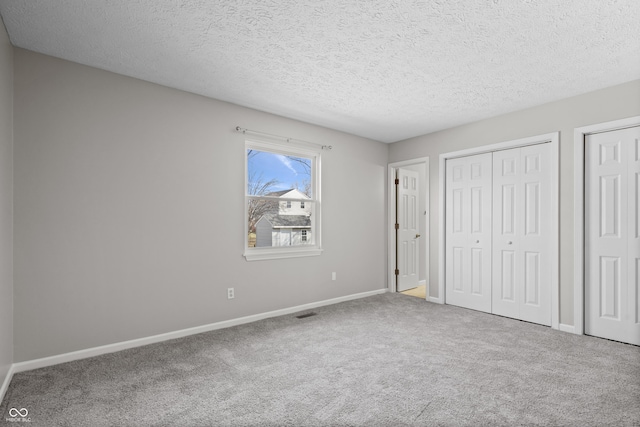 unfurnished bedroom featuring two closets, baseboards, carpet floors, and a textured ceiling