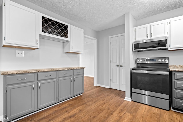 kitchen with baseboards, wood finished floors, gray cabinets, and stainless steel appliances