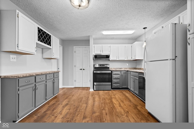 kitchen with wood finished floors, gray cabinets, stainless steel appliances, a textured ceiling, and decorative light fixtures