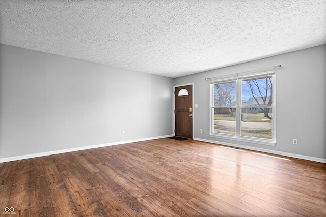 unfurnished living room featuring baseboards, wood-type flooring, and a textured ceiling