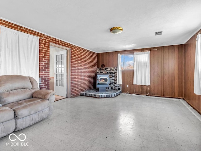 unfurnished living room with visible vents, brick wall, wood walls, light floors, and a wood stove