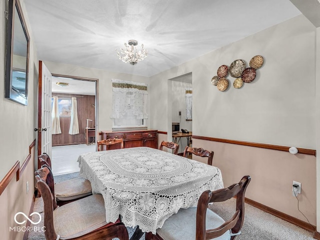 carpeted dining space featuring a chandelier and baseboards