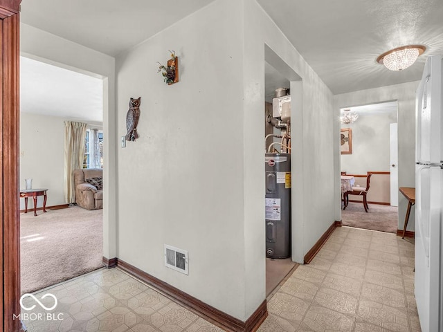 hall featuring visible vents, light colored carpet, electric water heater, baseboards, and light floors