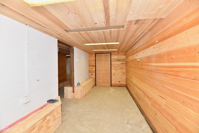 hallway featuring wooden walls, concrete flooring, and wooden ceiling