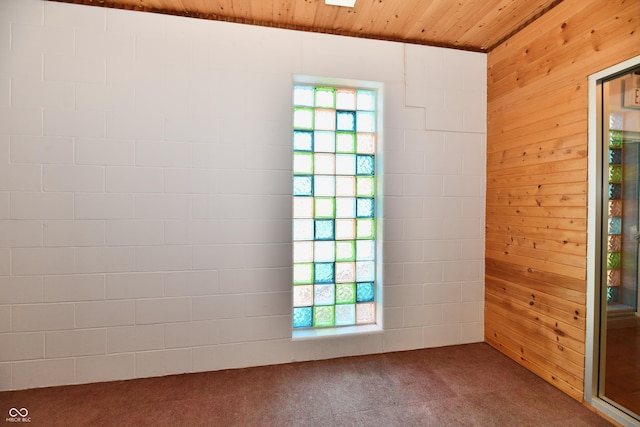 carpeted spare room with wooden ceiling and wood walls