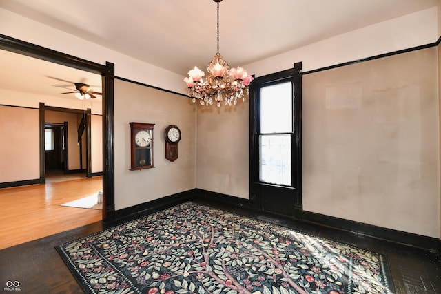 unfurnished room with ceiling fan with notable chandelier, baseboards, and wood finished floors